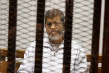 FILE - In this file photo taken Thursday, May 8, 2014, Egypt's ousted Islamist President Mohammed Morsi sits in a defendant cage in the Police Academy courthouse in Cairo, Egypt. Besides the current charges against him of conspiring with foreign groups, inciting the murder of his opponents and orchestrating prison breaks during the 2011 uprising that toppled his predecessor, Hosni Mubarak, Egypt's state prosecutor is now investigating allegations that Morsi leaked secret documents to Qatar via the Doha-based Al-Jazeera broadcaster, judicial officials said Wednesday, Aug. 27. (AP Photo/Tarek el-Gabbas, File)