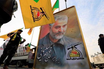 Des combattants du Kataeb Hezbollah portent des drapeau de ce groupe à côté d'un portrait du général  Qassem Soleimani. (Archives)